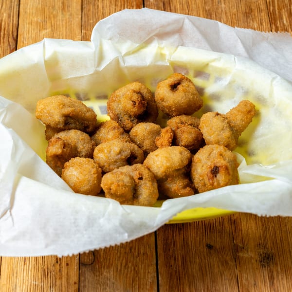 A yellow basket lined with white paper holds a generous serving of golden-brown fried mushrooms.