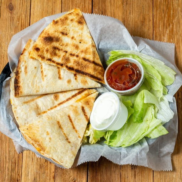 Grilled quesadilla wedges with salsa, sour cream, and lettuce in a basket on a wooden table.