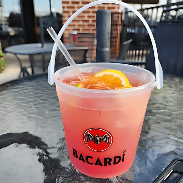 A large Bacardi bucket cocktail with a lemon slice and straw on a glass table outdoors.